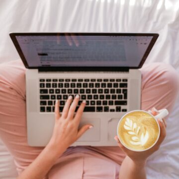 A woman's hands with a coffee working on a laptop.